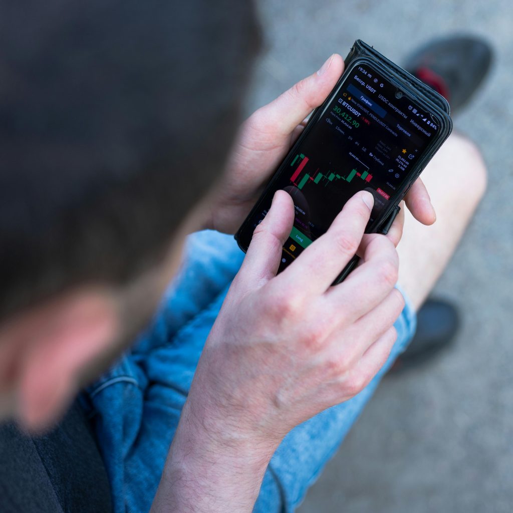 A man in casual attire checks cryptocurrency prices on his smartphone outdoors.