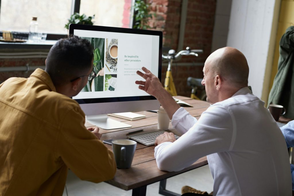 Two colleagues collaborating on a project in a modern office setting with a computer display and coffee.