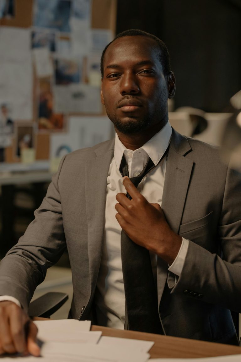Businessman adjusting tie at office desk with documents, conveying confidence and professionalism.