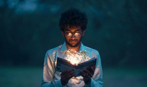 pexels-photo-2781195-2781195 A man with glasses reads an illuminated book outdoors during twilight.