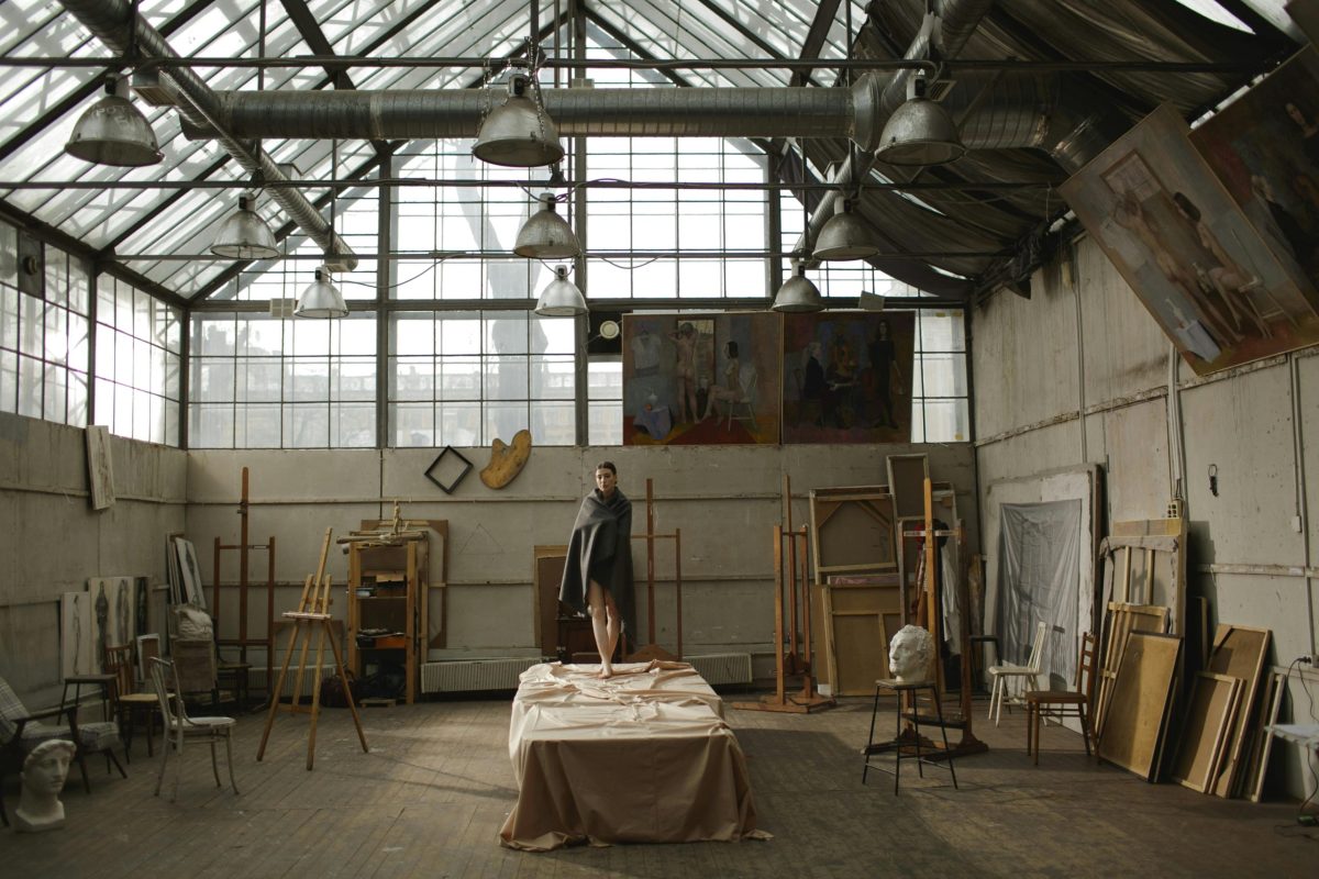 pexels-photo-3778571-3778571 A model stands on a table amidst artistic clutter in a spacious, sunlit studio.