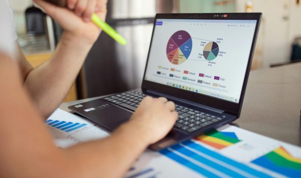 pexels-photo-7948060-7948060 Person analyzing financial charts and graphs on a laptop with colorful documents, showcasing market analysis.