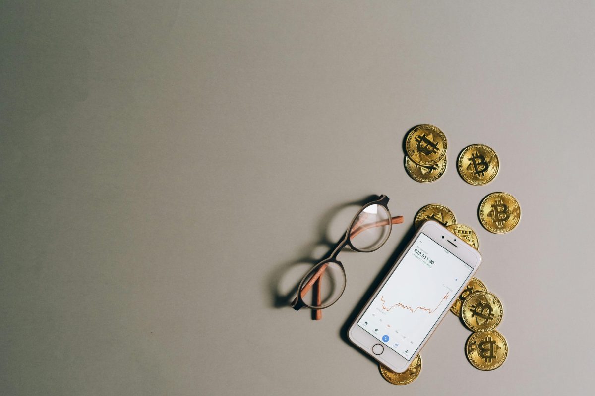 pexels-photo-8919551-8919551 Flat lay of Bitcoin coins, smartphone with graph, and glasses on gray surface.